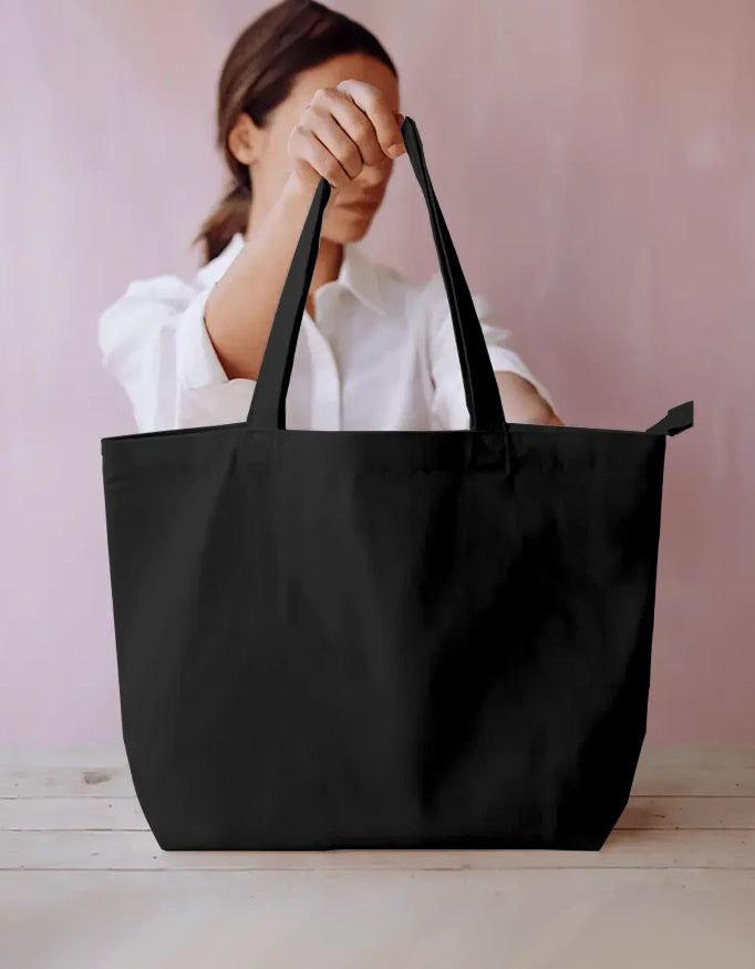 Oversized black tote bag with handles displayed by a woman in a white shirt on a light table