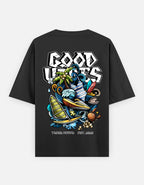 A TREND FEVER black short-sleeve t-shirt with a large, colorful graphic print on the back. The graphic features the text 'GOOD VIBES' in a stylized white font above an illustration of a surfer, waves, a green plant, and other coastal elements.