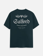 A dark teal short-sleeve t-shirt with a white graphic print on the front featuring the text 'Salford URBAD STREETWEAR' and 'TREND FEVER ESTD 2024' under a winged logo, displayed on a light gray background.