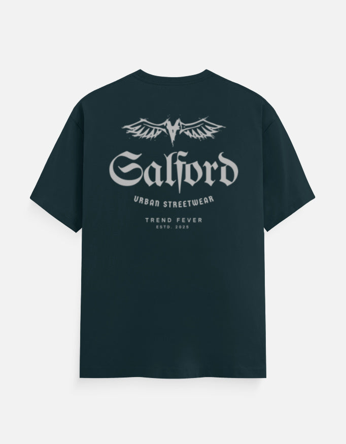 A dark teal short-sleeve t-shirt with a white graphic print on the front featuring the text 'Salford URBAD STREETWEAR' and 'TREND FEVER ESTD 2024' under a winged logo, displayed on a light gray background.