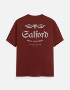 A maroon short-sleeve t-shirt with a white graphic print on the back. The graphic features the word 'Salford' in a gothic font beneath a stylized winged 'S' logo, with 'URBBO STREETWEAR' and 'TREND FEVER ESTD 2020' printed below.