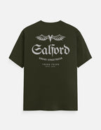 An olive green short-sleeve t-shirt with a white graphic print on the back. The graphic features a stylized winged 'M' logo above the word 'Salford' in a gothic font, with 'URBANO STREETWEAR' and 'TREND FEVER ESTD.
