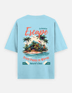 A light blue short-sleeve t-shirt shown from the back, featuring a colorful graphic print of a tropical island with palm trees and text that reads 'Escape', 'From Peaks to Waves', and 'Nature's Best'.