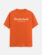 An orange short-sleeve t-shirt with 'Brotherhood' printed in a white gothic font across the chest, and smaller text underneath reading 'THING FEVER ESTD. 2020', shown on a light gray background.