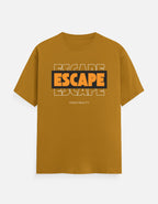 A mustard yellow short-sleeve t-shirt with a graphic on the chest reading 'ESCAPE' in orange and black, with 'FROM REALITY' printed below, displayed on a light gray background.