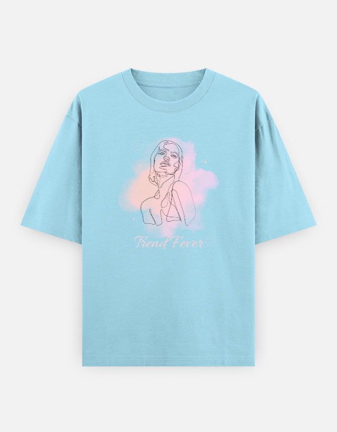 A light blue short-sleeve t-shirt with a graphic of a woman's line art over a pink and purple watercolor background, with the text 'Trend Fever' printed below.