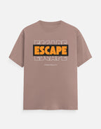 A dusty rose short-sleeve t-shirt with a graphic on the chest featuring the word 'ESCAPE' in orange and black, layered over a faint white outline of the same word, with 'FROM REALITY' printed below in small white text.