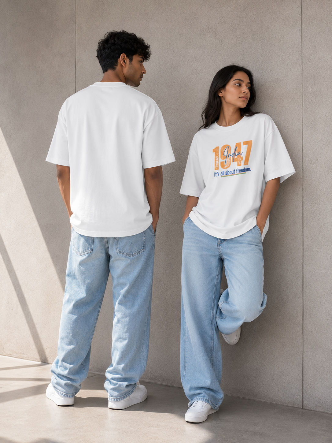 Two models wearing Trend Fever oversized white graphic t-shirts and light blue jeans, standing against a textured concrete wall.