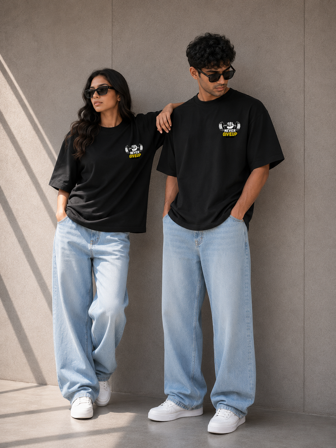 A man and a woman wearing Trend Fever matching black graphic T-shirts with light-wash wide-leg jeans and white sneakers, standing against a textured gray wall.