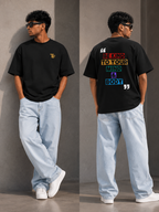 A man modeling a TREND FEVER black graphic T-shirt in a split front and back view. The front features a small yellow 'TF' logo on the left chest, while the back displays a colorful graphic with the text 'BE KIND TO YOUR MIND & BODY' in yellow, orange, green, and blue, framed by white quotation marks.