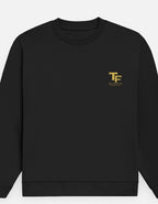 A black crewneck sweatshirt with a small gold 'TF' logo and 'TREND FEVER' printed on the left chest, displayed against a light gray background.