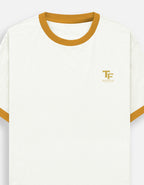 An off-white ringer t-shirt with a mustard yellow crew neck and sleeve trim, featuring a small gold 'TF' logo with 'TREND FEVER' underneath on the left chest.