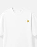 A white short-sleeve crewneck T-shirt featuring a small gold 'TF' monogram Trend Fever logo on the left chest, displayed against a clean white background.