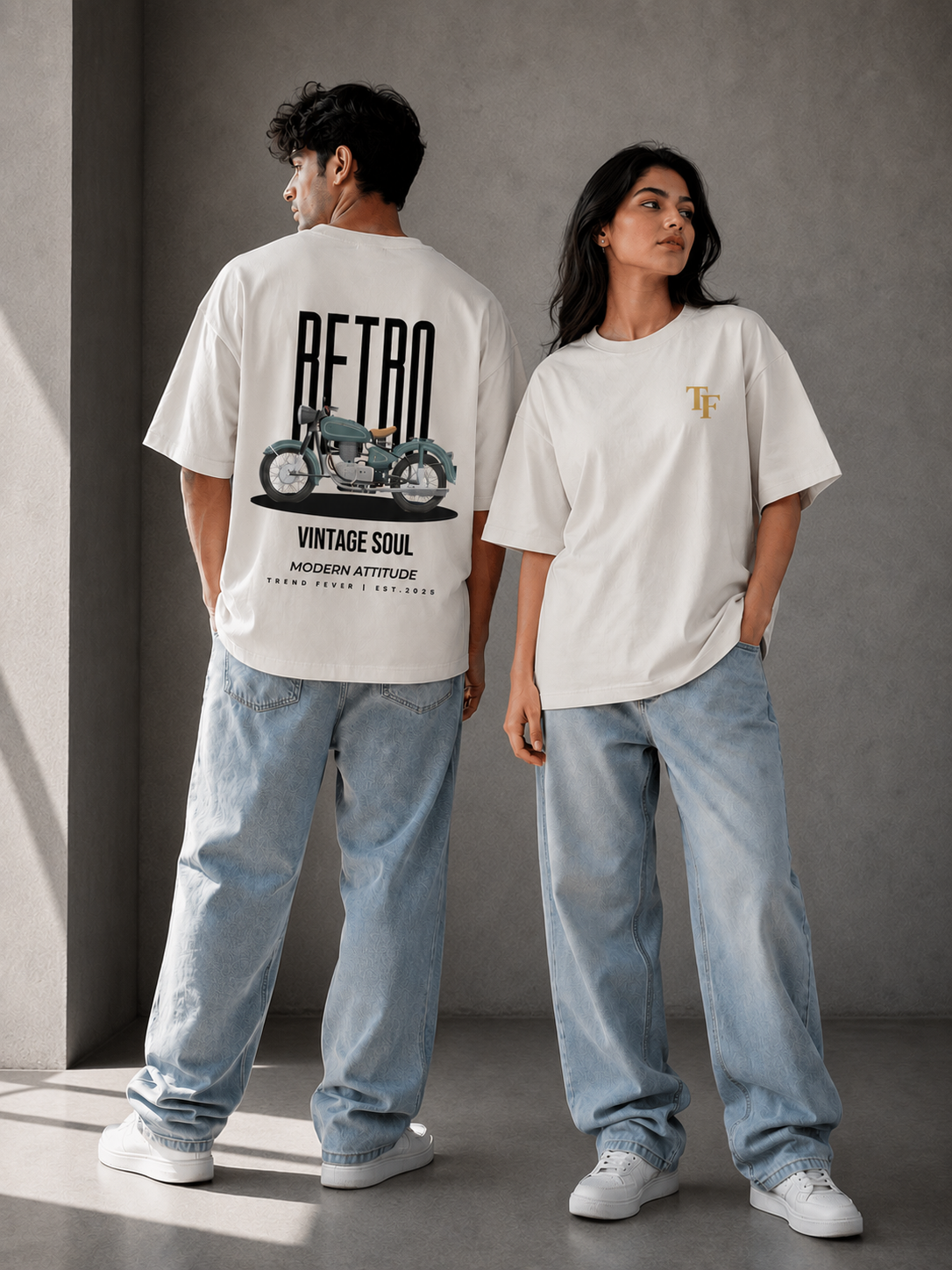 Two models wearing oversized white graphic t-shirts and light blue jeans standing in a minimalist gray studio setting. The model on the left shows the back of the shirt with a large black 'RETRO' graphic and motorcycle print, while the model on the right shows the front with a small gold 'TF' logo on the chest.