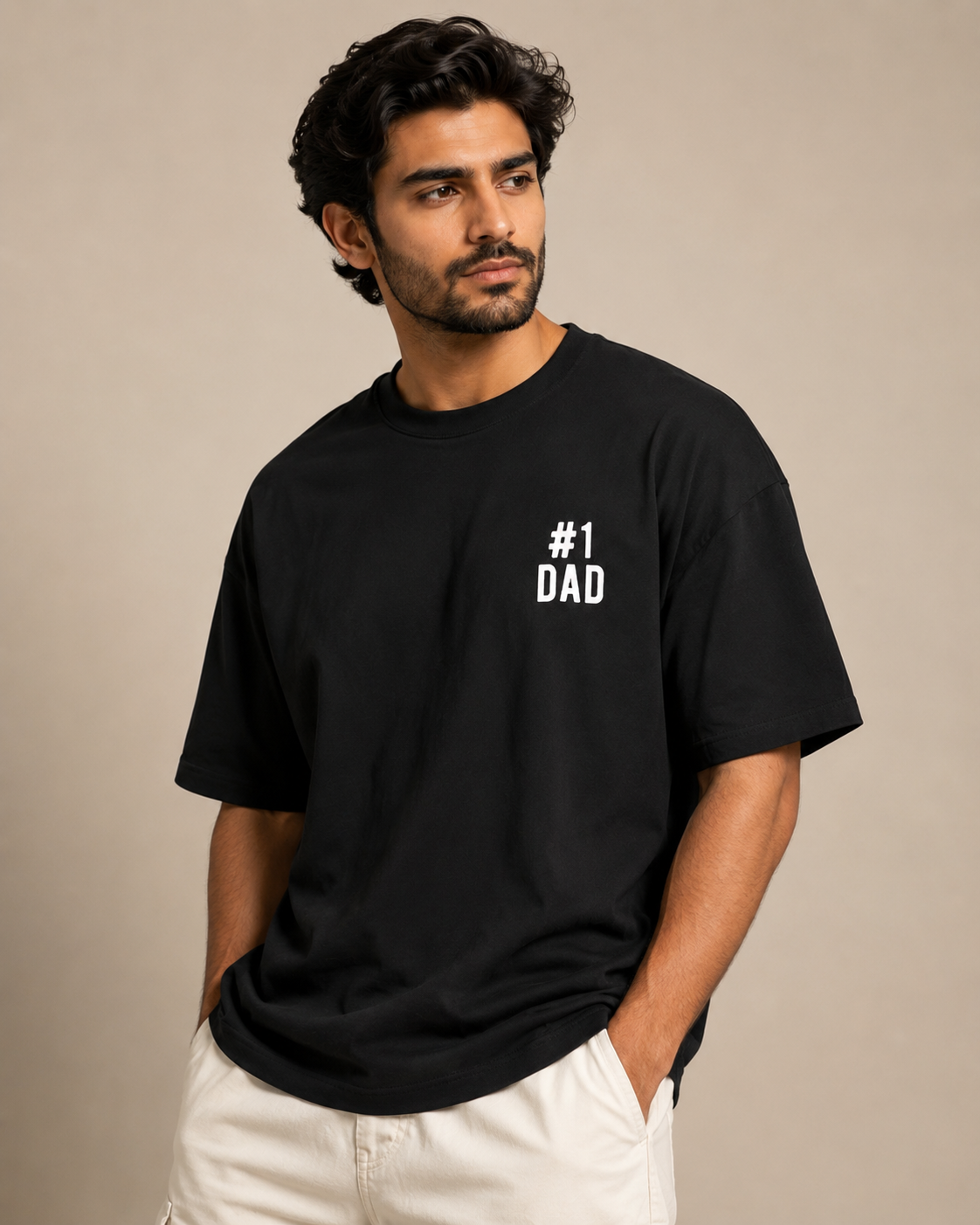 A man wearing a black Trend Fever crewneck t-shirt with the text '#1 DAD' printed in white on the left chest, paired with off-white pants, set against a plain beige background.
